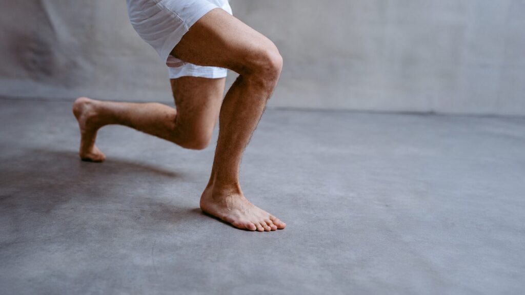 Person performing a forward lunge exercise barefoot to improve running strength, balance, and lower body mobility during physiotherapy.
